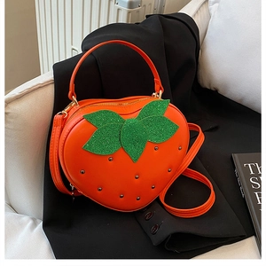 Détail d'un sac orange en forme de fraise avec feuilles pailletées et rivets argentés