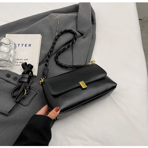 Detail of black leather small square bag on grey blazer with gold metal buckle