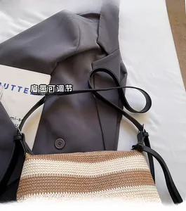 Detail of adjustable black leather strap on a beige and coffee striped woven shoulder bag