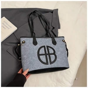 Close-up of a blue tote bag with black leather trim and round logo patch detailing