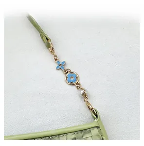 Detail of gold metal chain strap with blue floral charms and pearl on green woven bag