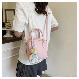 Detail of pink lychee textured crossbody bag with cute teddy bear charm accessory