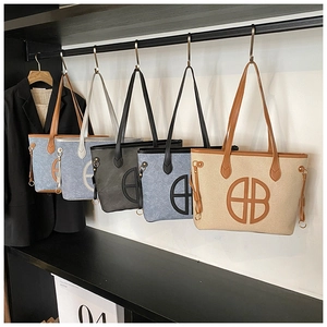 Row of large fabric tote bags with leather trim and round logo in five diverse colors