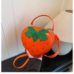 Détail du sac à main orange en forme de fraise avec feuilles pailletées et rivets noirs