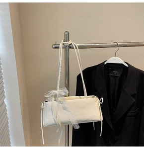 Detail of white baguette bag with delicate lace ribbon and bow on black suit background