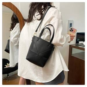 Détail du sac seau en cuir noir avec coutures géométriques et boucles dorées sur modèle