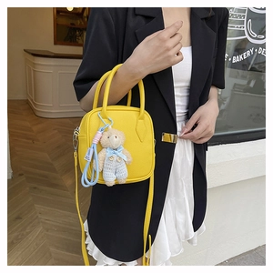 Detail of yellow pebbled leather handbag featuring a cute plush bear charm on the side