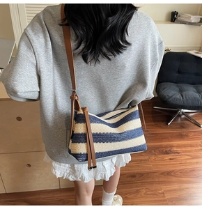 Detail of striped woven crossbody bag with brown leather strap and tassel charm