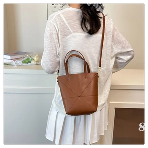 Détail d'un sac seau marron avec coutures géométriques porté par un mannequin de profil