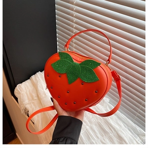 Détail du sac à main rouge en forme de fraise avec clous noirs et feuilles vertes pailletées