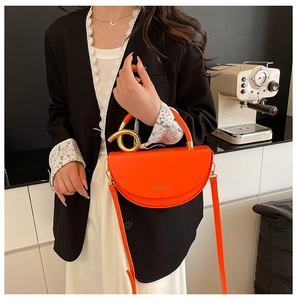 Detail of orange half-moon crossbody bag featuring artistic gold twisted metal handle