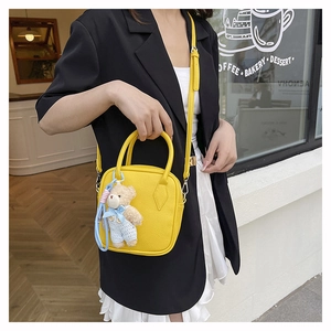 Detail of yellow pebbled leather handbag with cute teddy bear charm and round handles