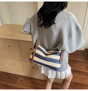 Detail of navy and white striped woven crossbody bag with brown leather strap on model