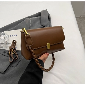 Detail of a brown leather crossbody bag with braided handle and gold metal lock buckle