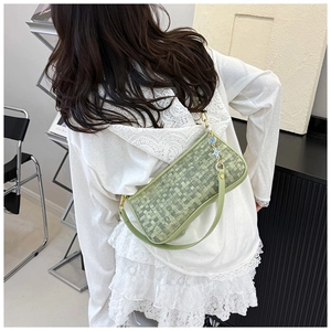 Detail of light green woven underarm bag with flower pendant worn by a model