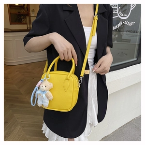 Detail of yellow pebbled leather crossbody bag featuring a cute plush bear charm