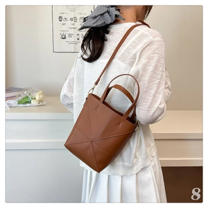 Sac seau en cuir marron avec coutures géométriques porté à l'épaule dans une pièce douillette