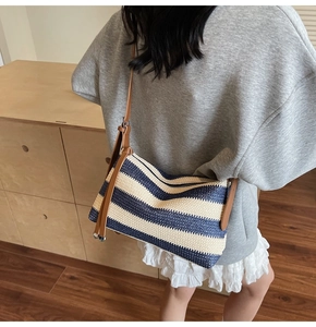 Detail of woven straw crossbody bag with blue stripes and adjustable brown strap
