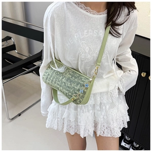 Detail of light green woven texture pillow bag with flower pendant and shoulder strap