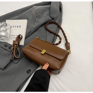 Detail of dark brown leather underarm bag with gold metal clasp on a grey suit jacket