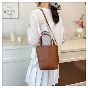 Détail du sac seau en cuir marron montrant les coutures en X et la bandoulière réglable