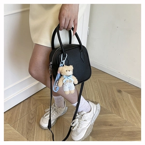 Detail of black textured crossbody square bag with a cute plush bear pendant accessory
