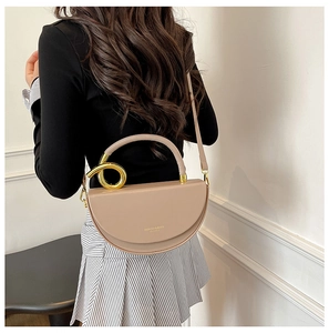 Detail view of beige half-moon handbag with gold ring handle and leather shoulder strap