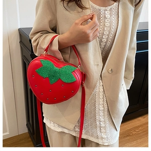 Détail du sac bandoulière en forme de fraise avec feuilles pailletées et lanière rouge