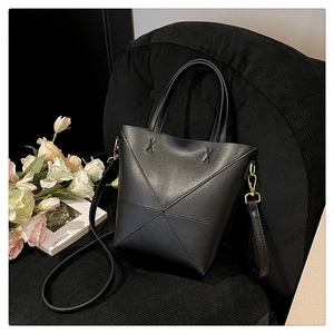 Détail du sac seau noir mat avec coutures géométriques sur une chaise en velours