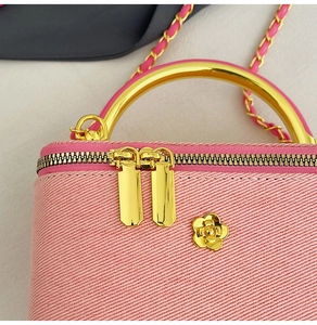Detail of pink tweed box bag featuring golden ring handle and camellia flower ornament