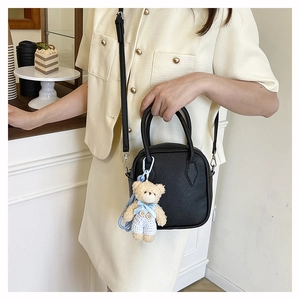 Close-up of black pebble leather square handbag with cute bear charm on a cafe counter