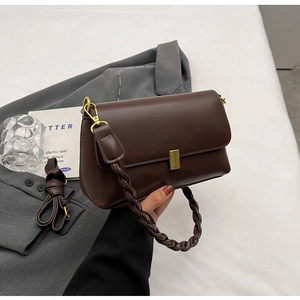 Detail of dark brown leather handbag with golden metal buckle and woven handle on a blazer