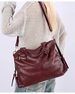 Detailed view of deep red vintage leather tote bag shown on a model's shoulder