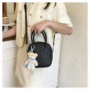 Detail of black lychee texture square bag with cute teddy bear plush charm and slim strap