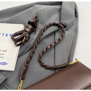 Detail of dark brown leather handbag with woven strap and gold clasp on grey fabric
