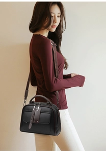 Detail of black leather handbag featuring dual zippers, rivets, and a wide shoulder strap