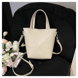 Détail d'un sac seau crème avec coutures géométriques en X et poignée supérieure