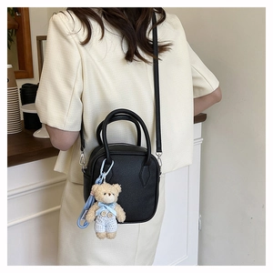 Detail of black pebbled leather square bag with a cute bear charm on a crossbody strap