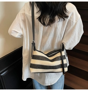 Detail of hand-woven straw crossbody bag with black and white stripes and leather strap