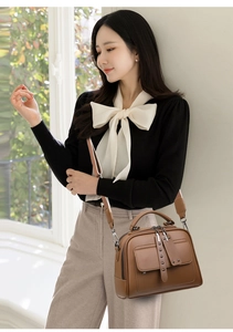 Brown leather handbag with adjustable strap shown worn by a model in a bright room