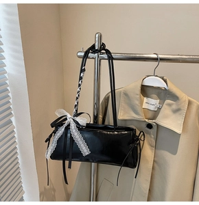 Detail of black glossy baguette bag with white lace bow hanging on a metal rack