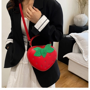 Détail du sac bandoulière fraise rouge avec paillettes vertes et rivets porté par un mannequin