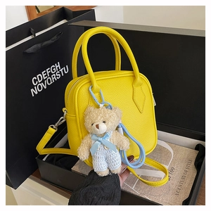 Detail of yellow pebbled leather square bag with cute teddy bear charm in a gift box