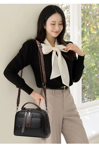 Classic black handbag with brown straps shown on model in a stylish indoor setting