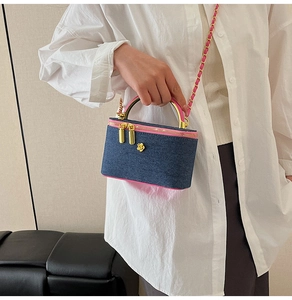 Detail showing blue denim box bag with pink leather trim and gold chain strap held by a model