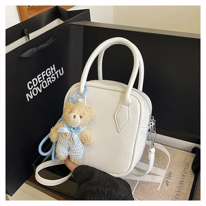 Close-up of white lychee leather texture on square crossbody bag with teddy bear charm