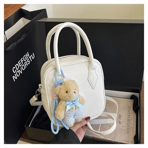White pebbled leather crossbody bag with cute plush bear charm in elegant gift box setup