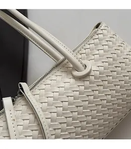 Detail shot of the woven leather texture and metal zipper on white shoulder bag