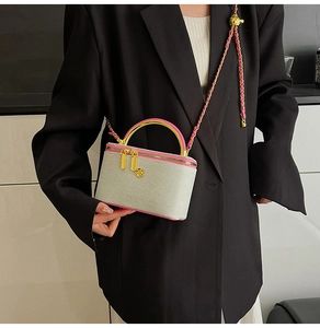 Detail of grey crossbody bag with pink trim, gold flower charm and chain strap