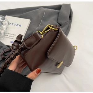 Detail of dark brown leather underarm bag featuring a woven strap and gold metal buckle